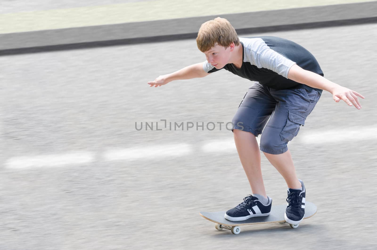 Young skater teenager guy in motion moving on skateboard along roadway against blurry asphalt background with copy-space area for text