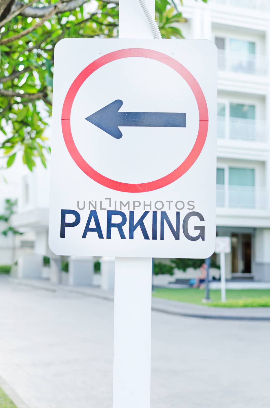 parking lot sign with left arrow and building in background by nopparats