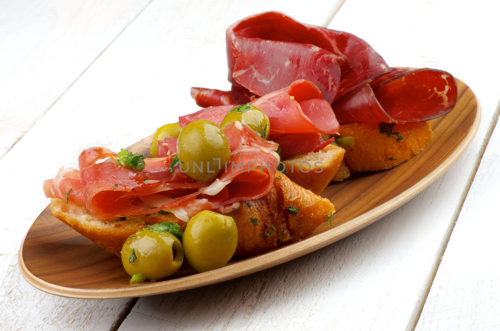 Delicious Tapas with Smoked Jamon, Cured Beef, Garlic Bread and Green Olives on Plate isolated on White Wooden background