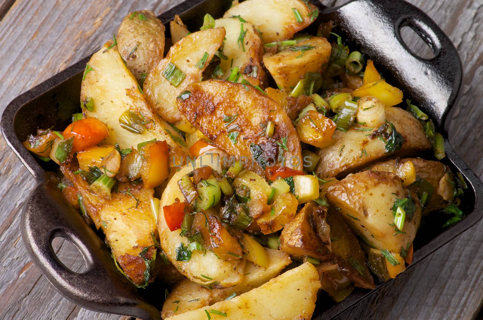 Rustic Roasted Potato Wedges with Greens and Paprika in Black Fry Pan closeup on Wooden background