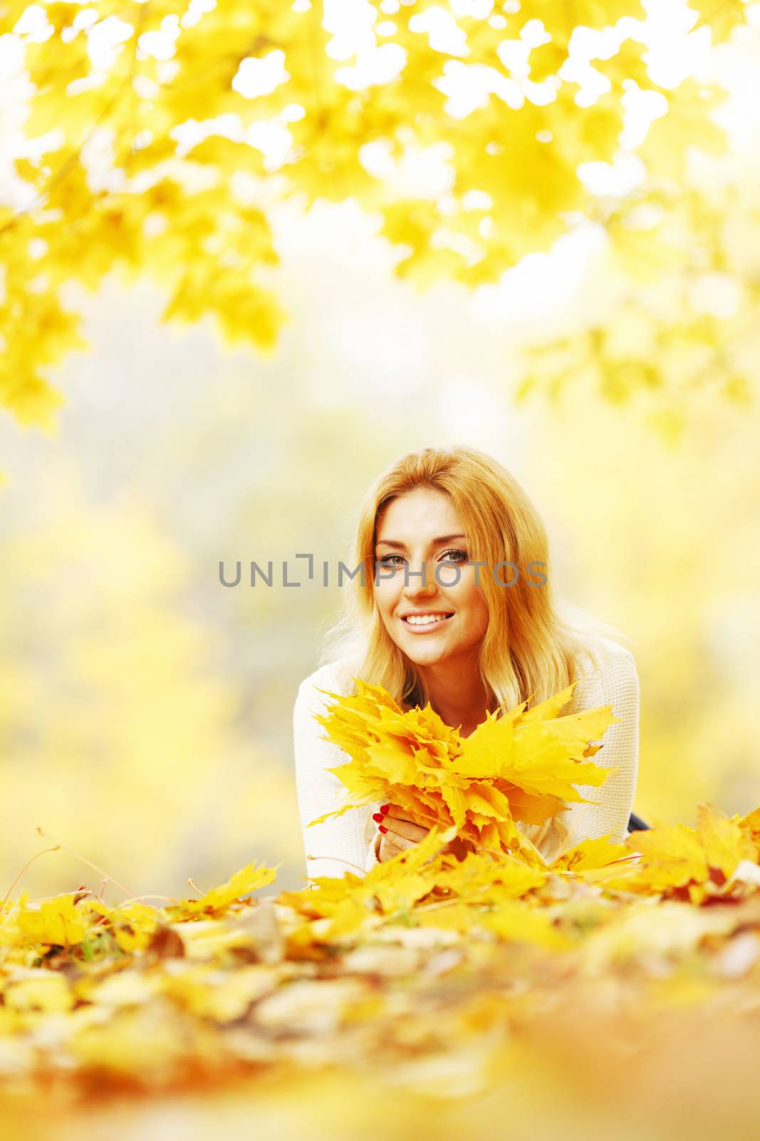 Young woman laying down on the ground covered dry autumnal foliage in beautiful park