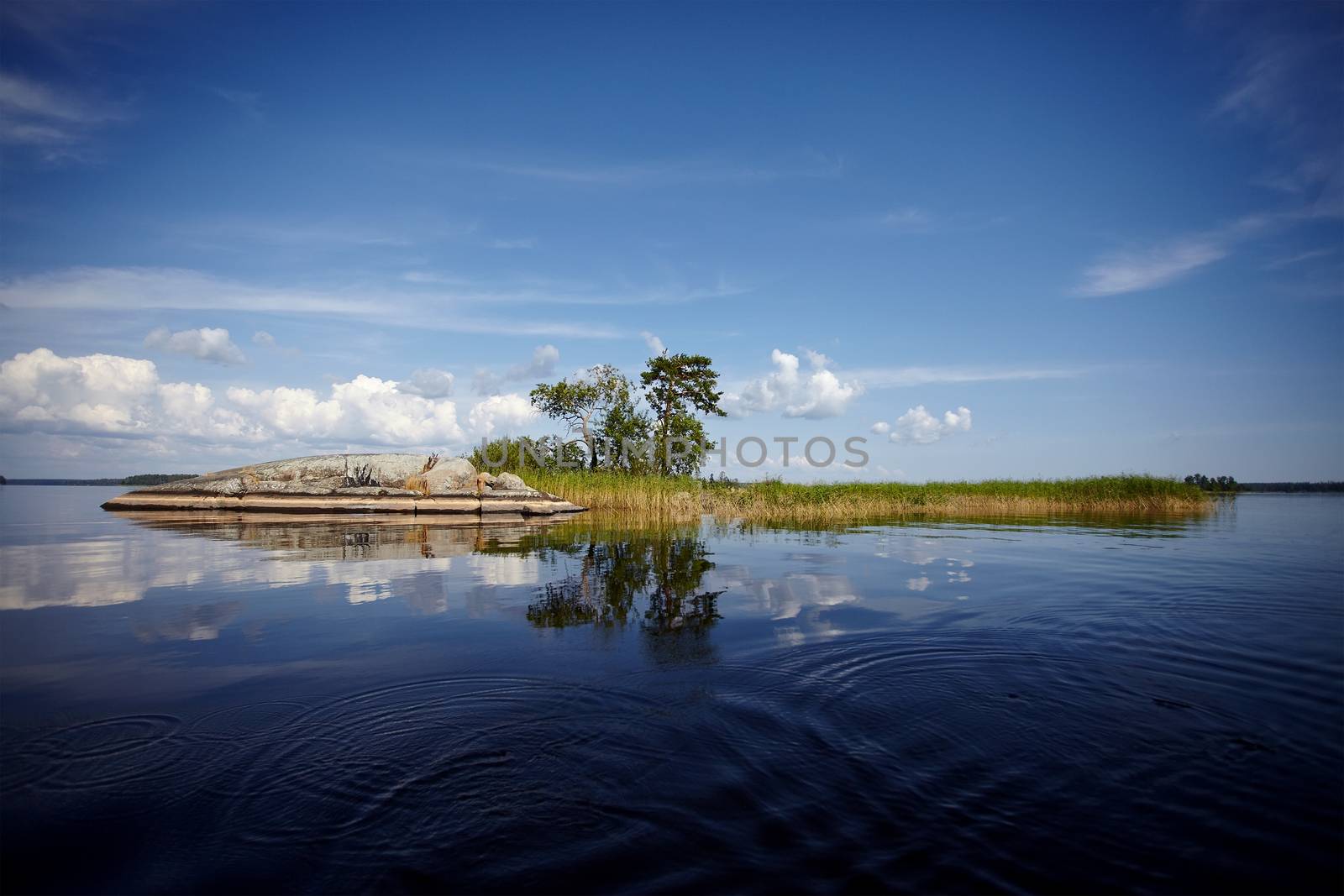Island in the lake. Water landscape with stones. Stones in water. The lake with stones. Beautiful landscape. Water smooth surface and the blue sky with clouds.