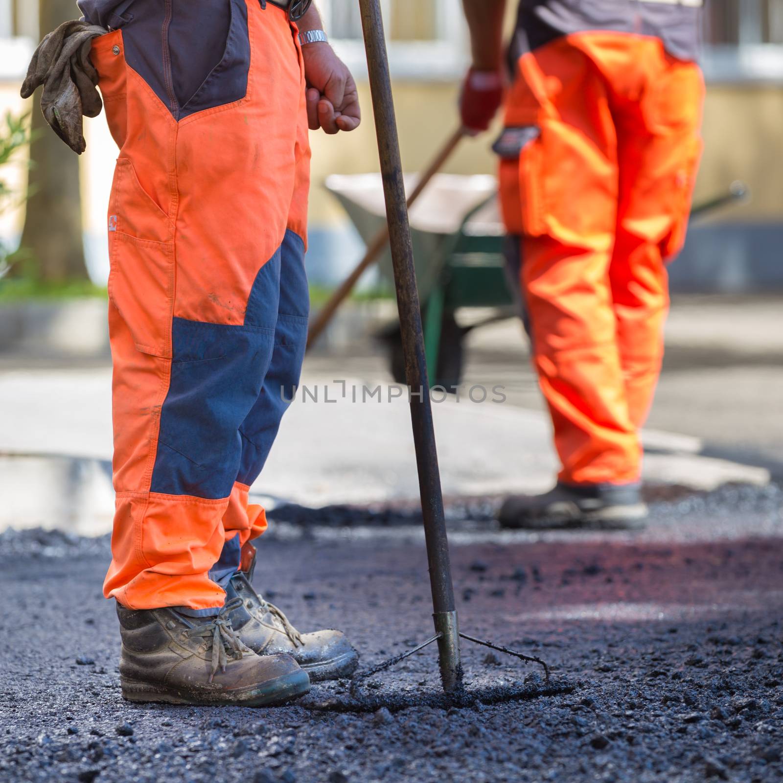 Construction workers during asphalting road works wearing coveralls. Manual labor on construction site.