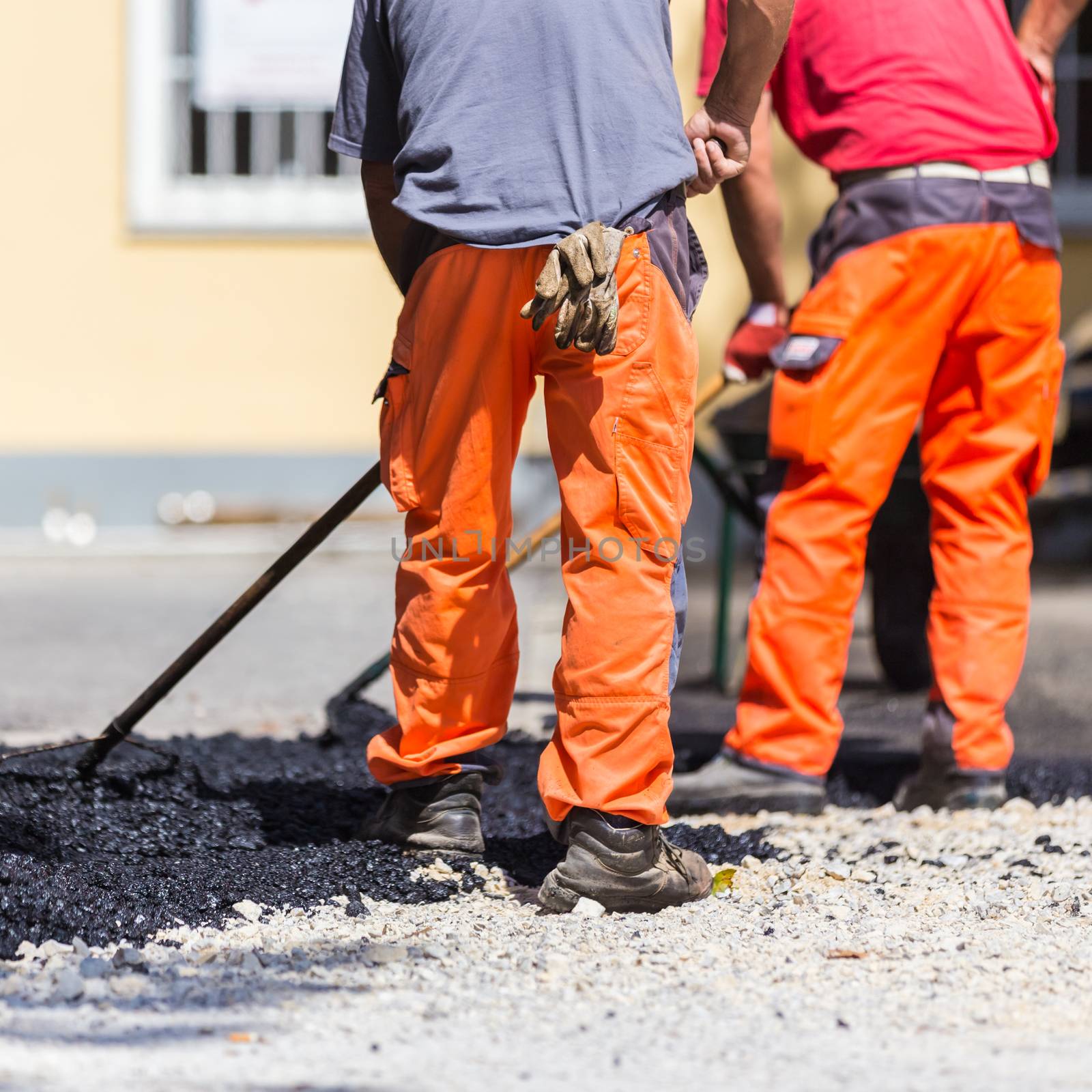 Construction workers during asphalting road works wearing coveralls. Manual labor on construction site.