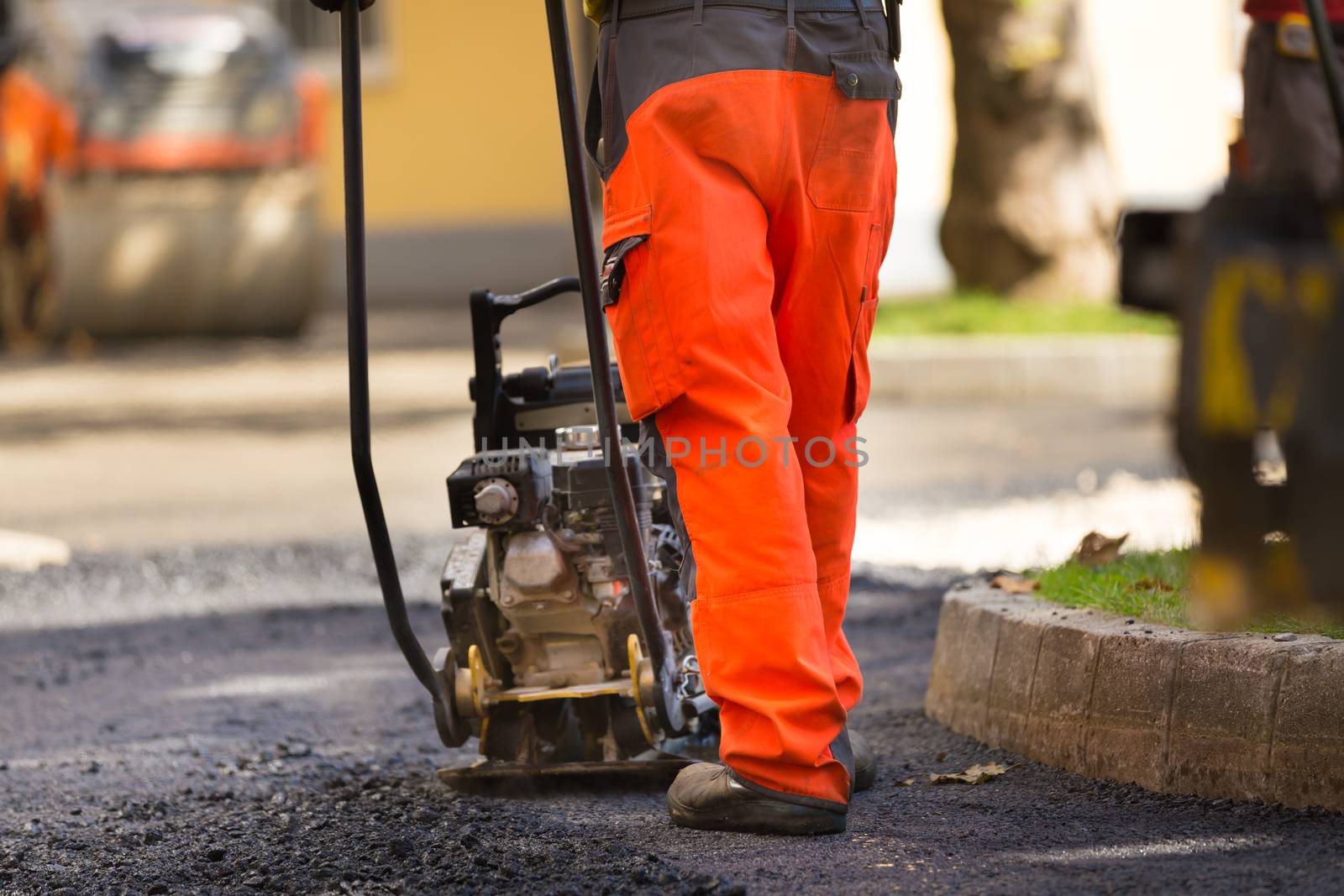 Construction workers during asphalting road works wearing coveralls. Manual labor on construction site.
