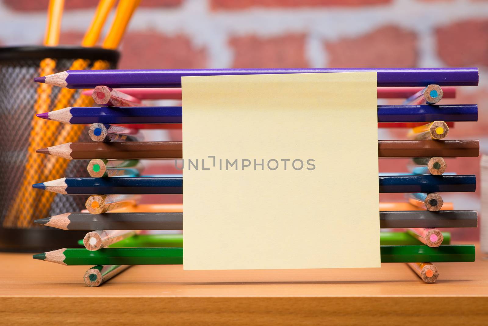 Desk with school supplies and colored pencil in front of brick wall 