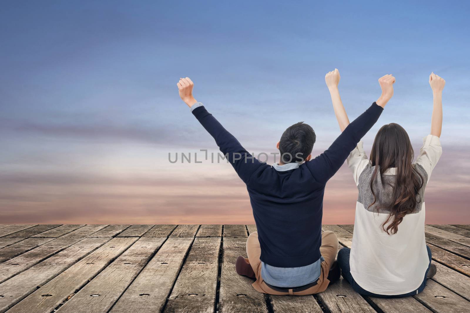 Asian couple sit on wooden ground and feel exciting against the dramatic sky with copyspace.