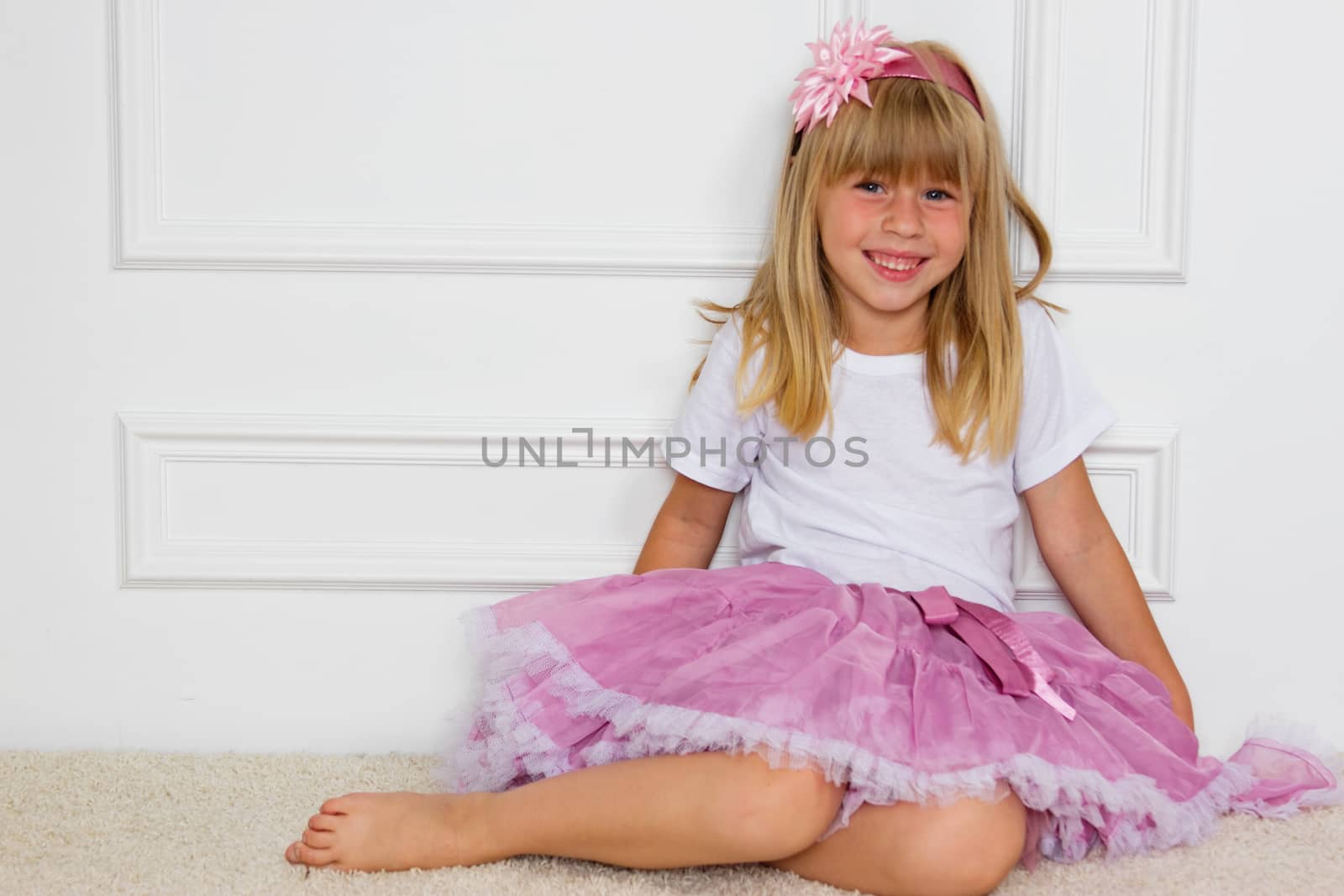 Little girl in a beautiful dress sits near a wall