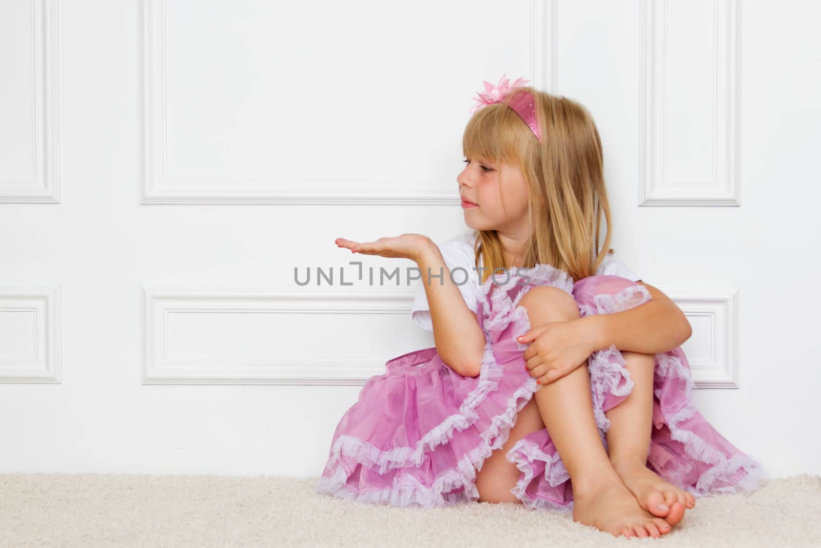 Little girl in a beautiful dress sits near a wall