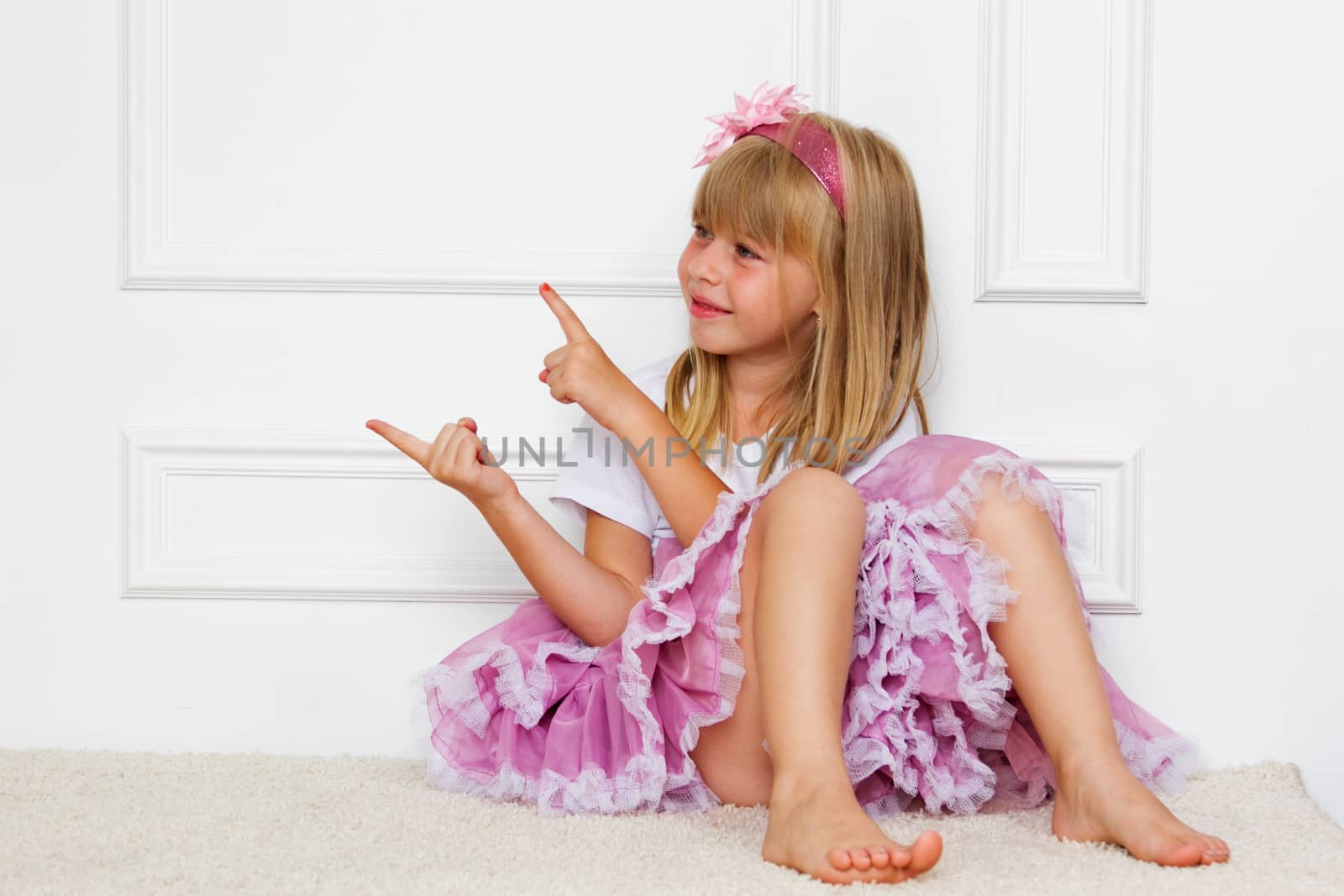 Little girl in a beautiful dress sits near a wall