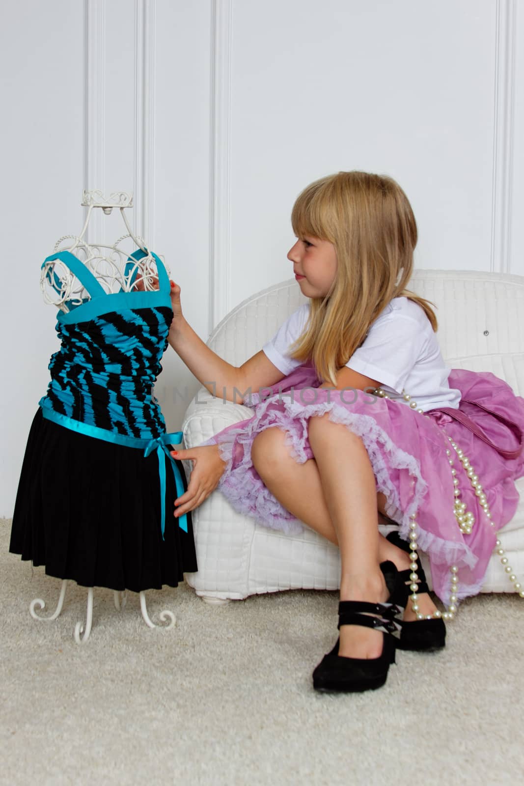 Girl in violet dress stands near mannequin in children store.