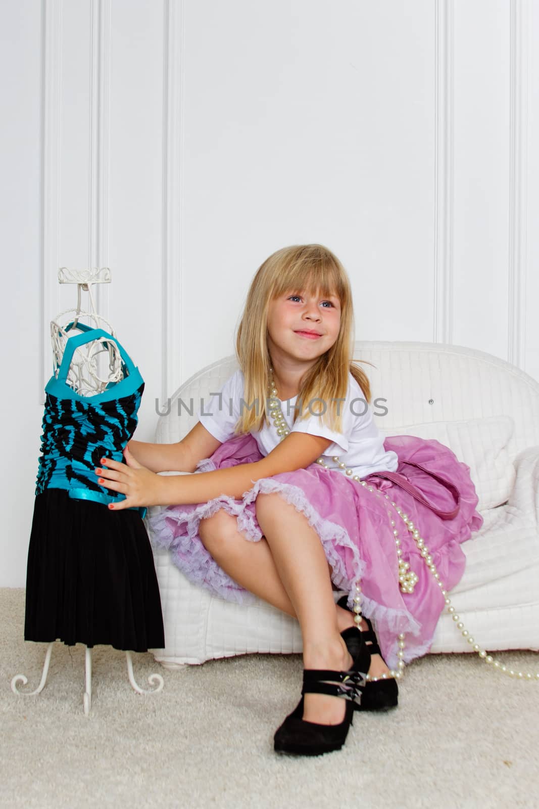 Girl in violet dress stands near mannequin in children store.