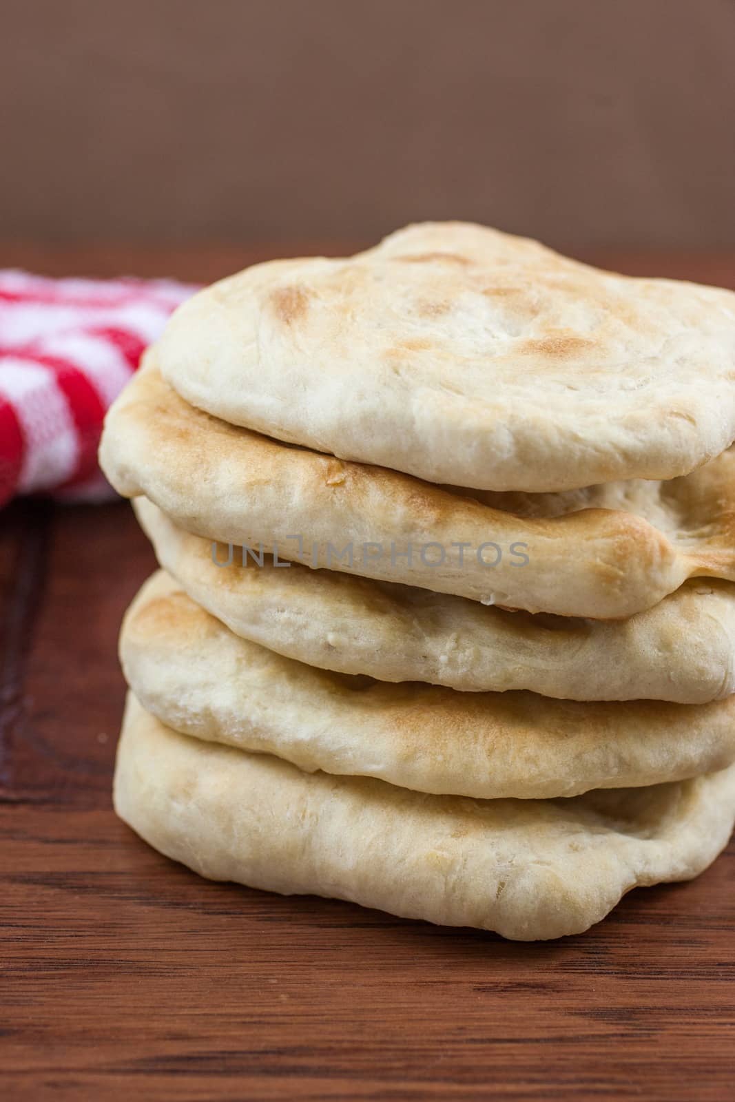 Homemade pita bread sitting on a wooden table with a red cloth in the background.