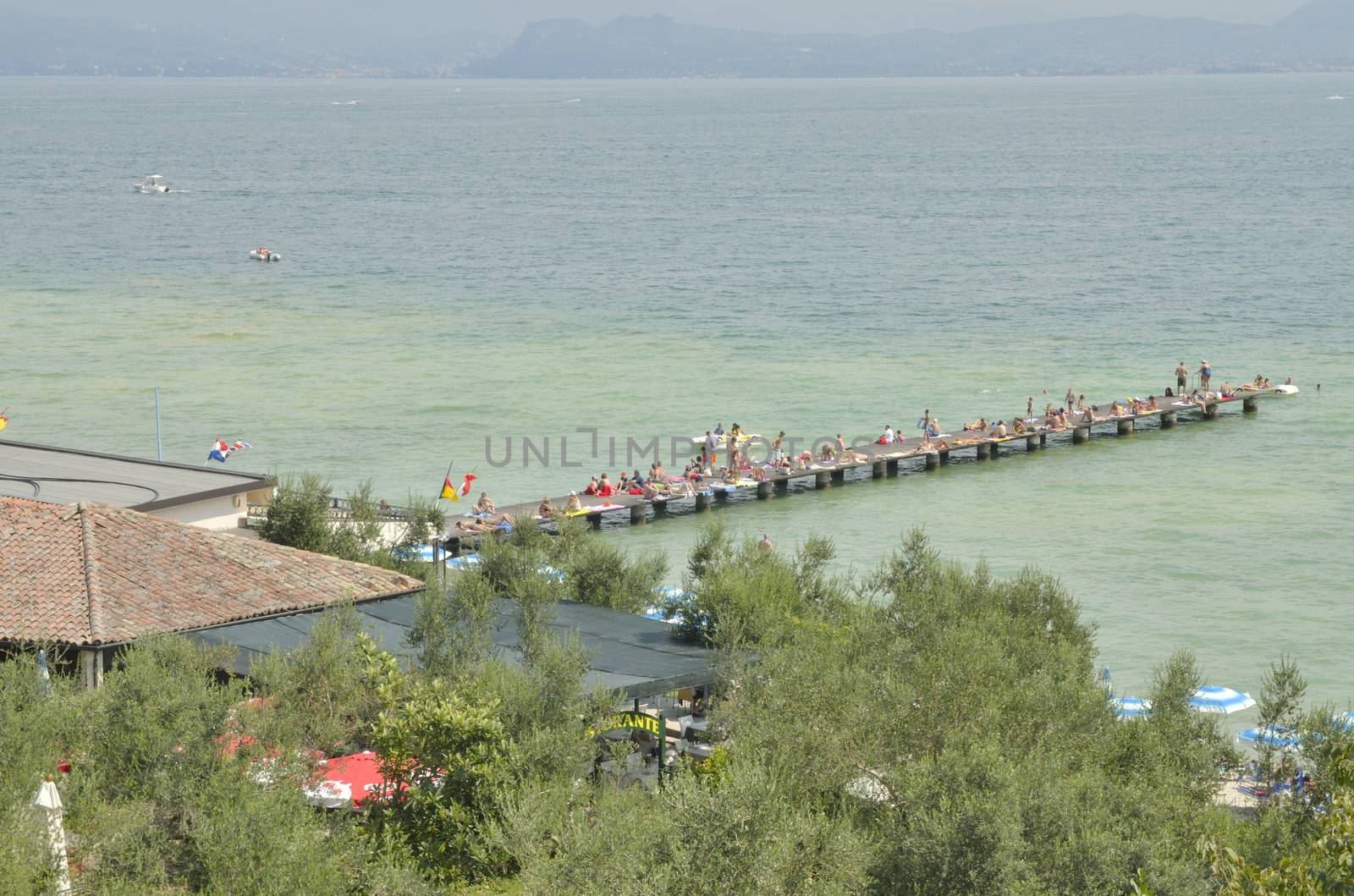 People sunbathing on wooden pier  in Sirmione, located in the lake Garda, Italy