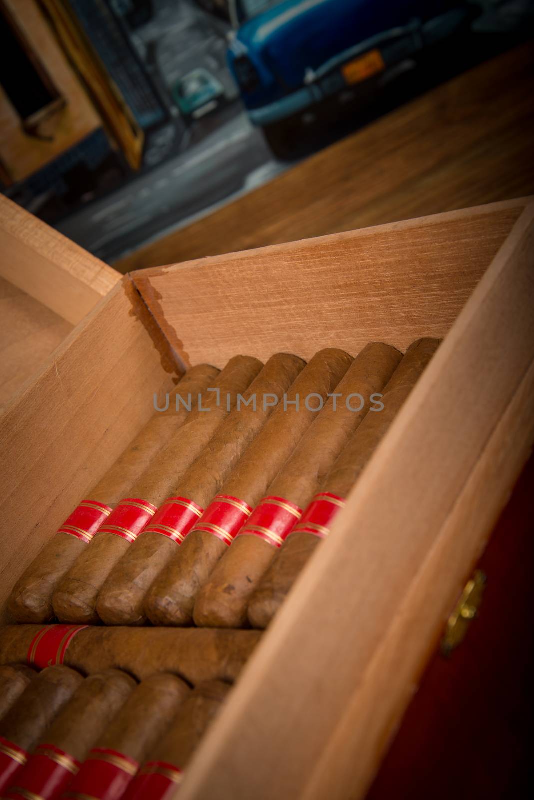 Cuban cigars and humidor on rustic wooden table with Cuban painting of american old car in background