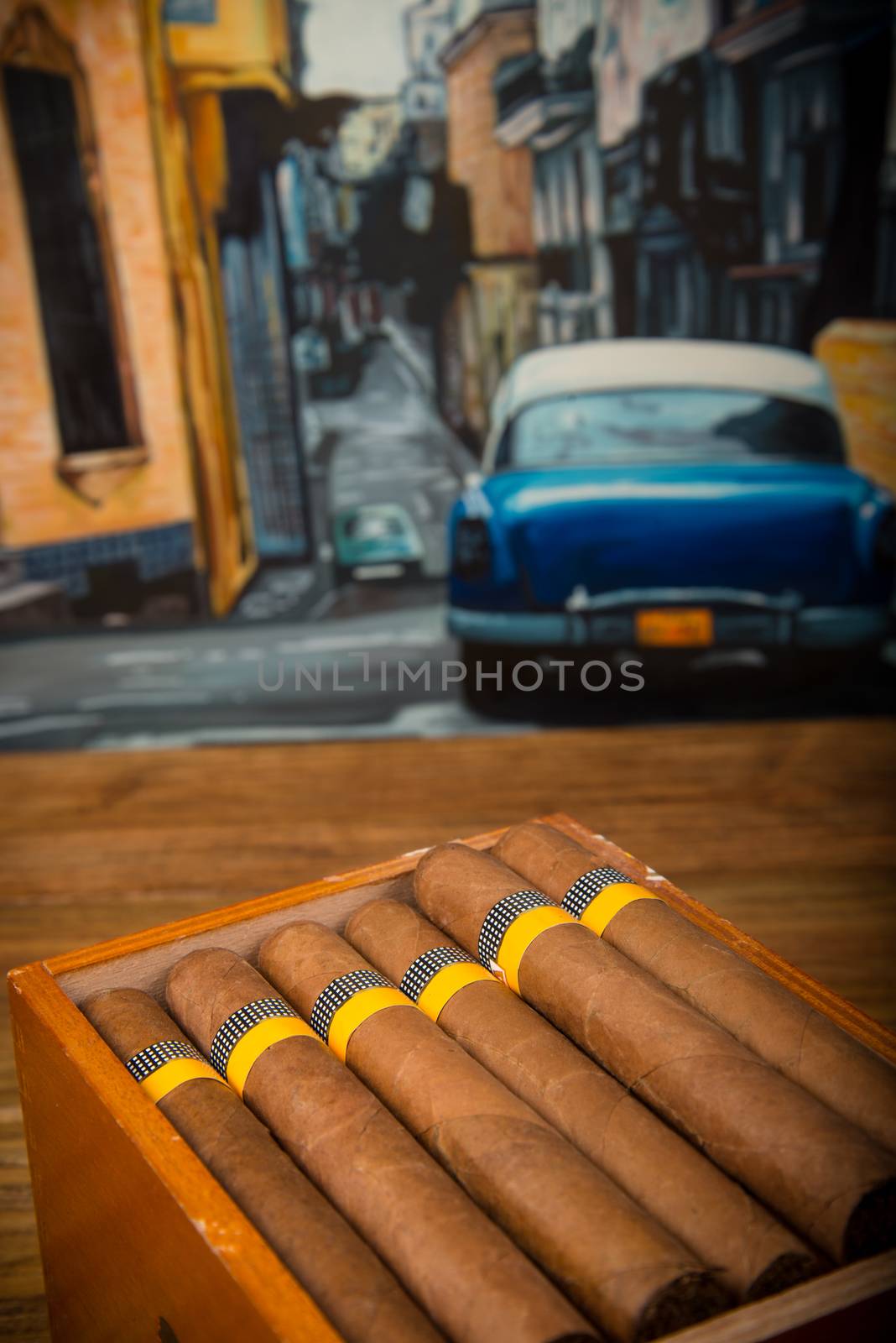 Cuban cigars and humidor on rustic wooden table with Cuban painting of american old car in background