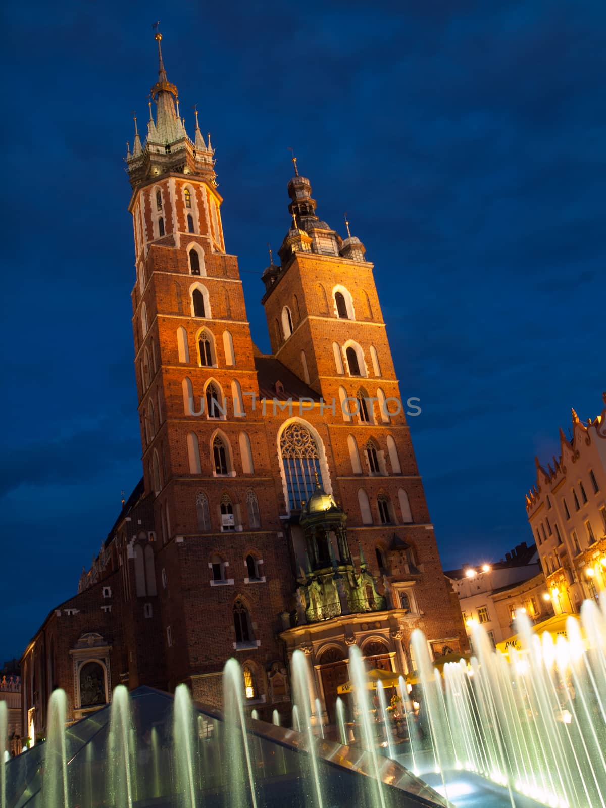 St. Mary's Church with two different towers by night (Krakow, Poland). Viewed from fountain.