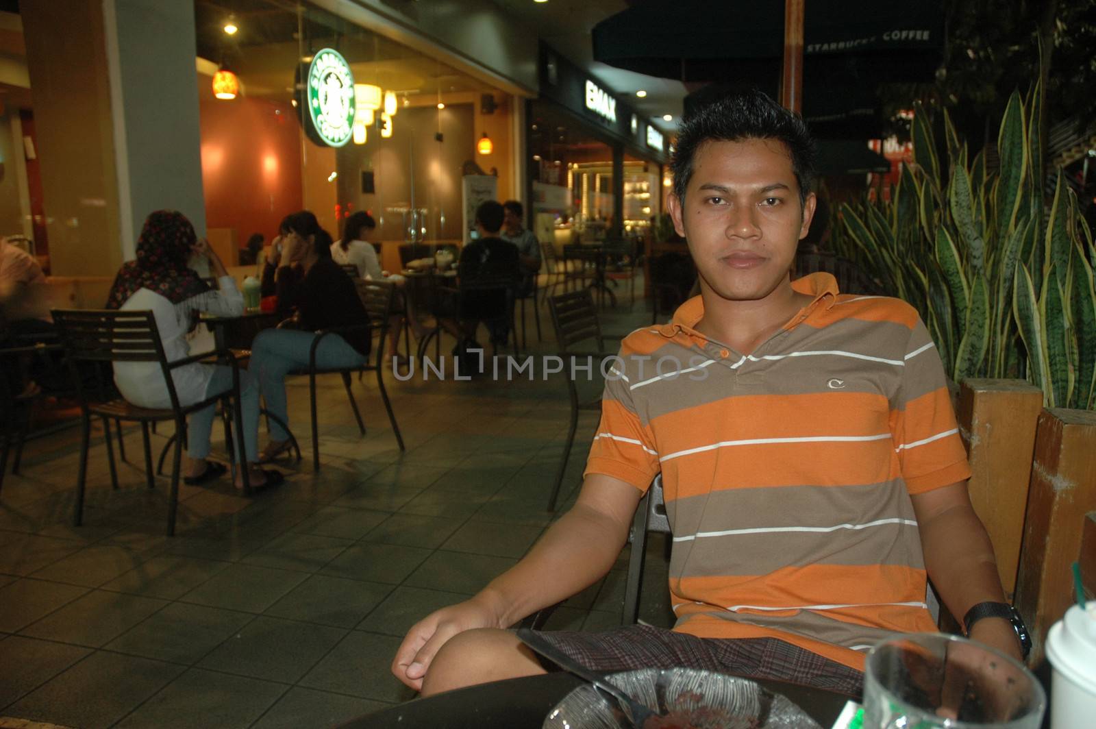 Bandung, Indonesia - July 2, 2011: Young man sit down on chair beside starbuck cafe.