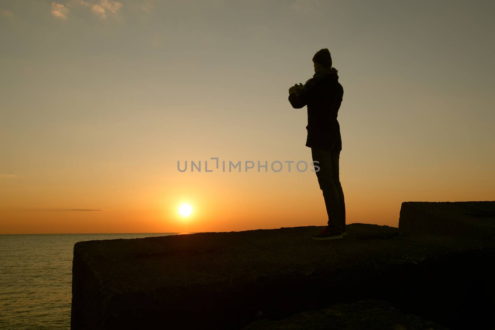 A man taking a photo of the sunset with his phone