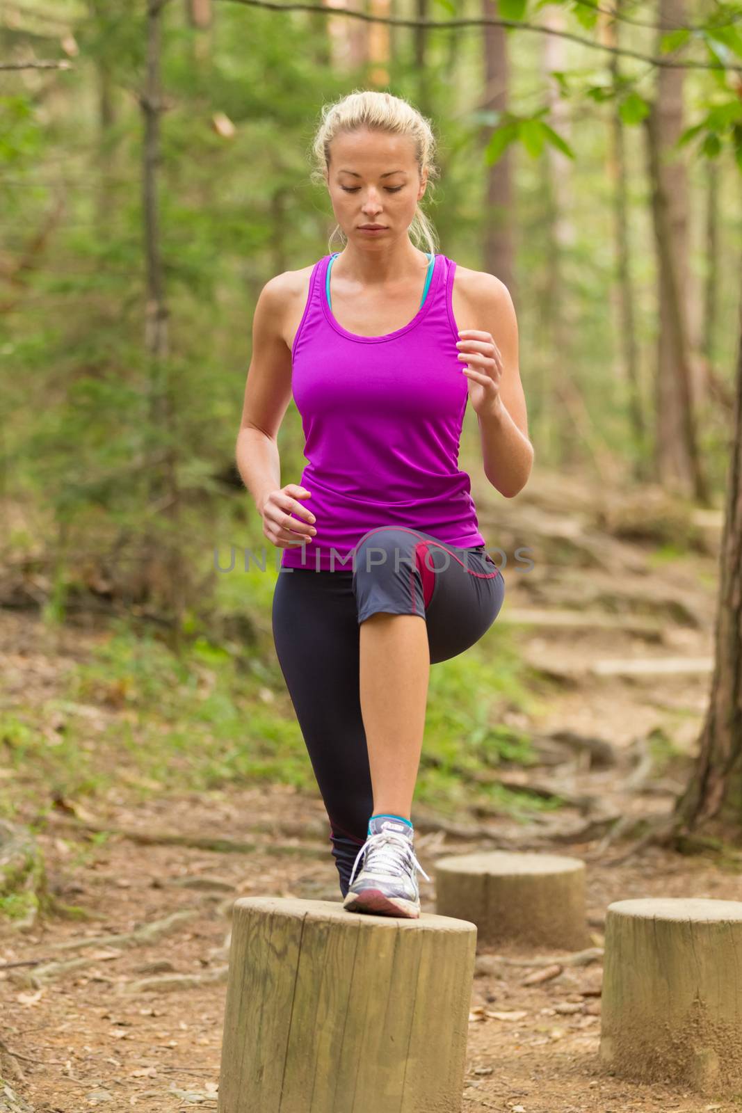 Young spotry woman doing cardio exercises on recreational trail outdoors in the park.