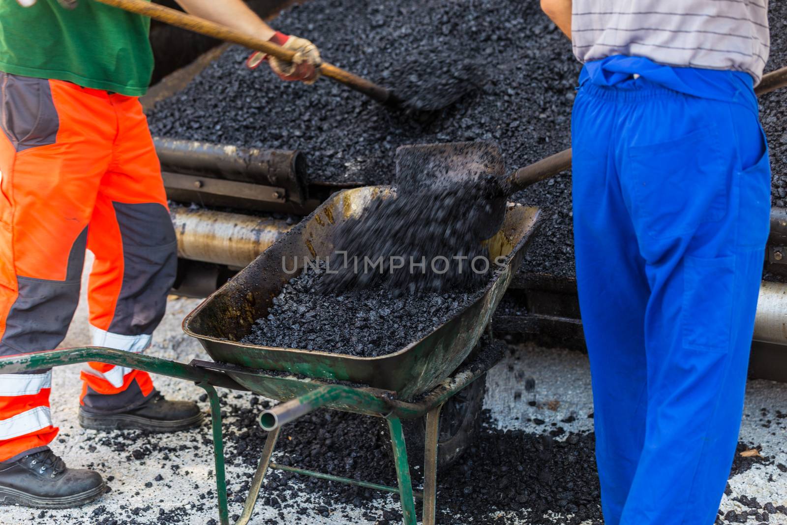 Construction workers during asphalting road works wearing coveralls. Manual labor on construction site.