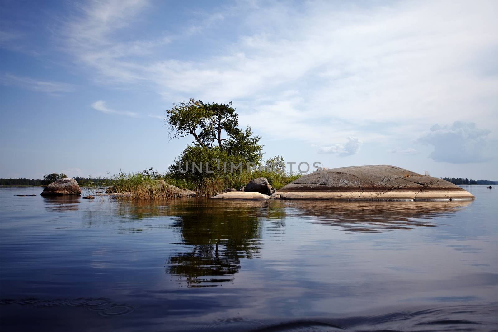 Island in the lake. Water landscape with stones. Stones in water. The lake with stones. Beautiful landscape. Water smooth surface and the blue sky with clouds.