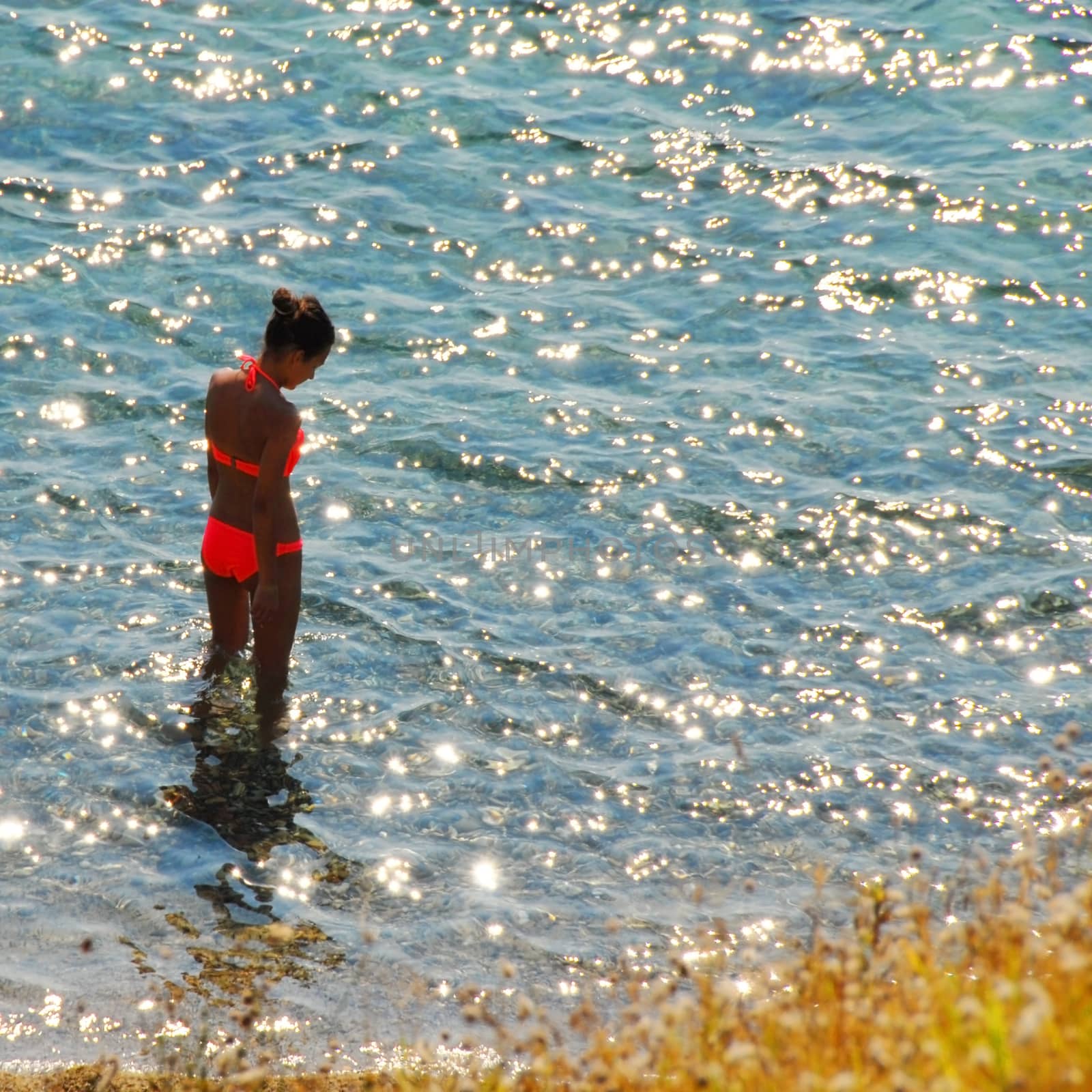girl in orange swimsuit over sunny shining sea water