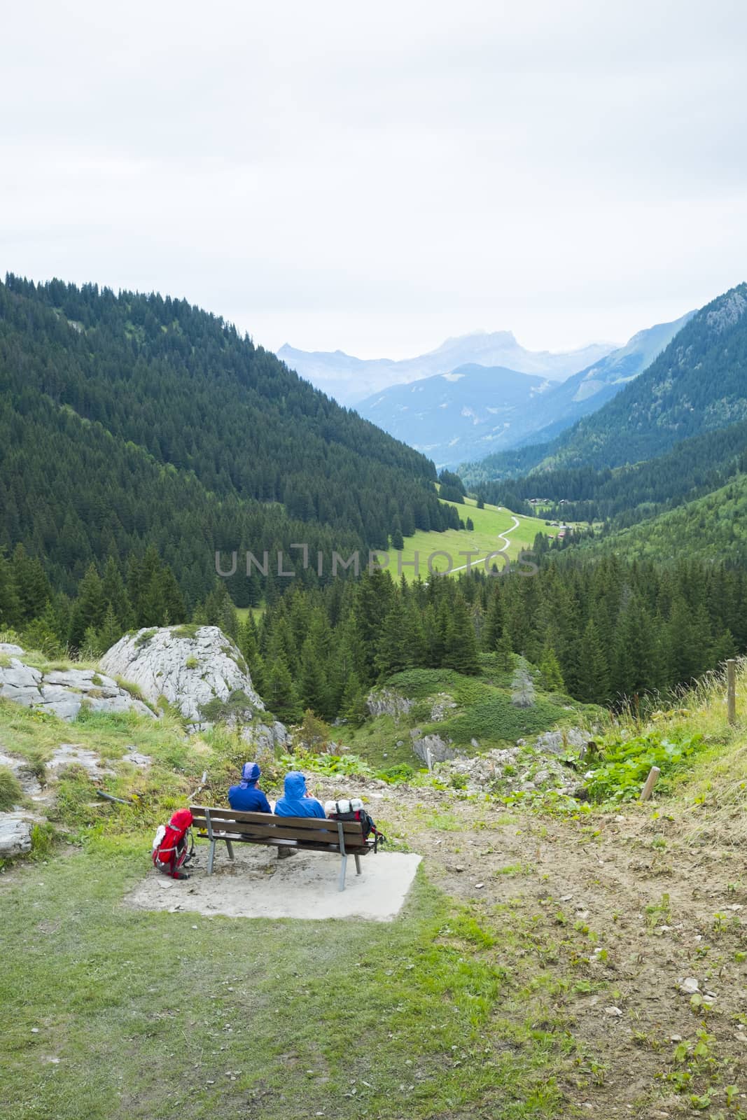 LA BALME, FRANCE - AUGUST 25: Hikers doing the Mont Blanc tour resting on bench in La Balme overlooking La Rollaz. The tour crosses France, Italy and Switzerland. August 25, 2014 in La Balme.