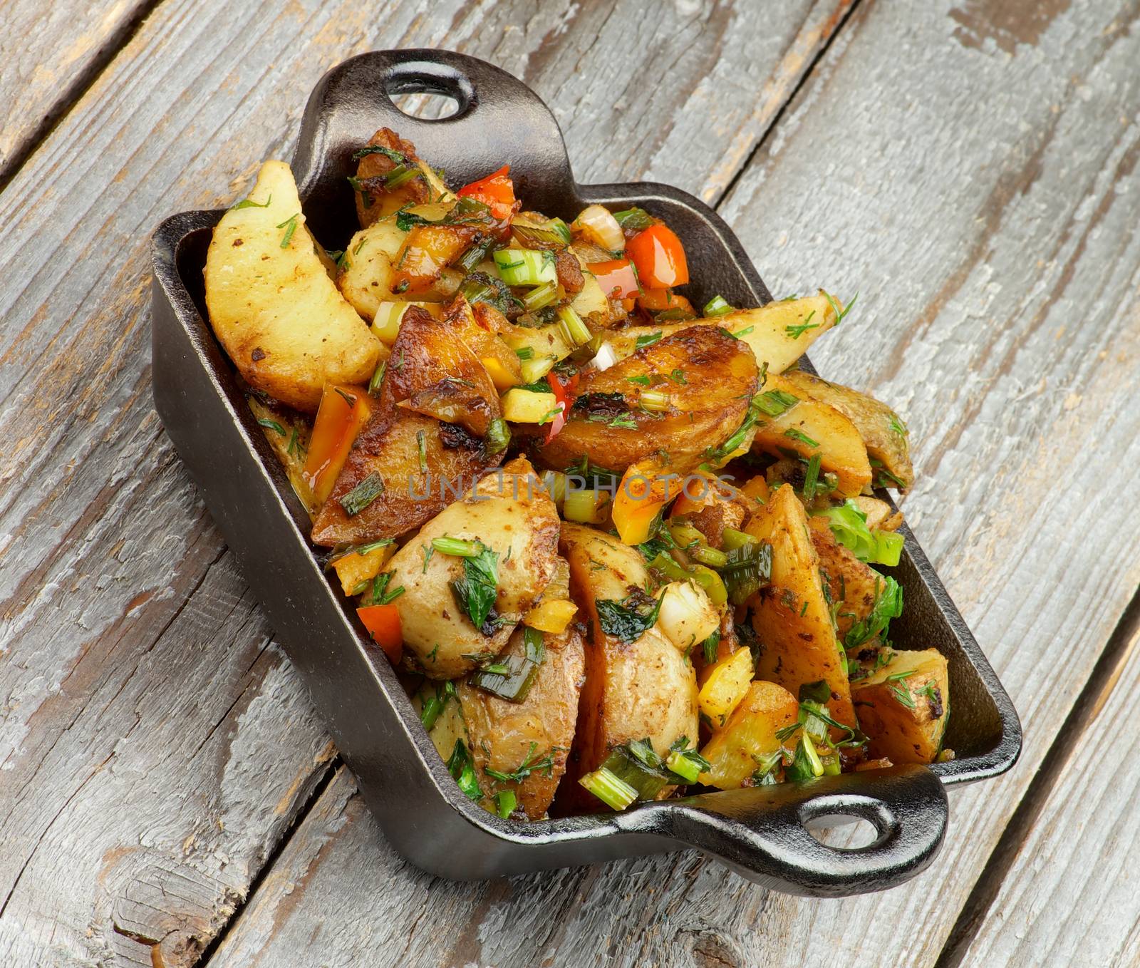 Roasted Potato Wedges with Greens and Paprika in Black Fry Pan isolated on Rustic Wooden background