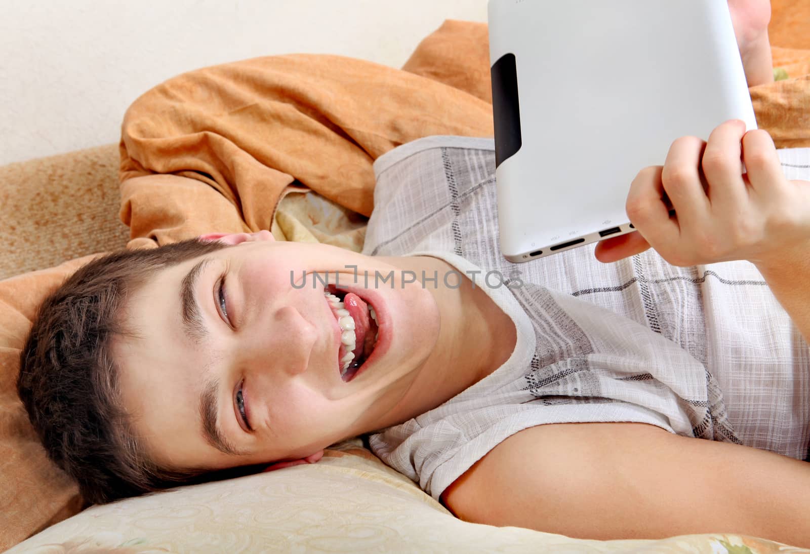 Cheerful Teenager with the Tablet Computer on the Sofa at the Home