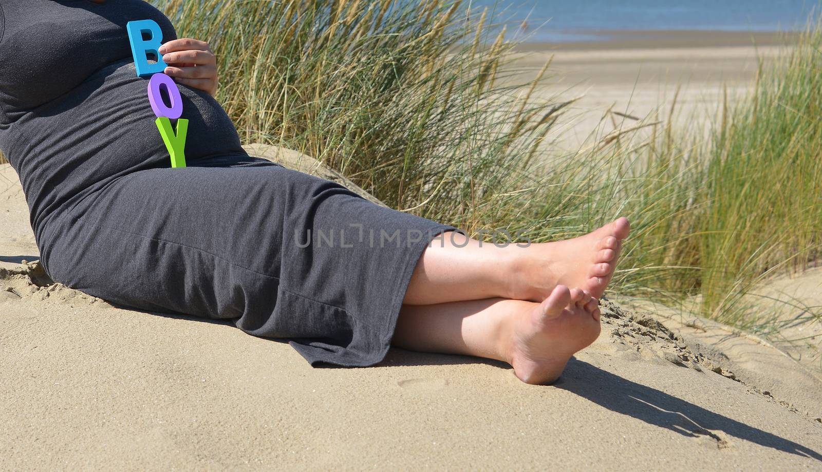 adult pregnant woman holding her hands on her belly on the beach with sand and sea