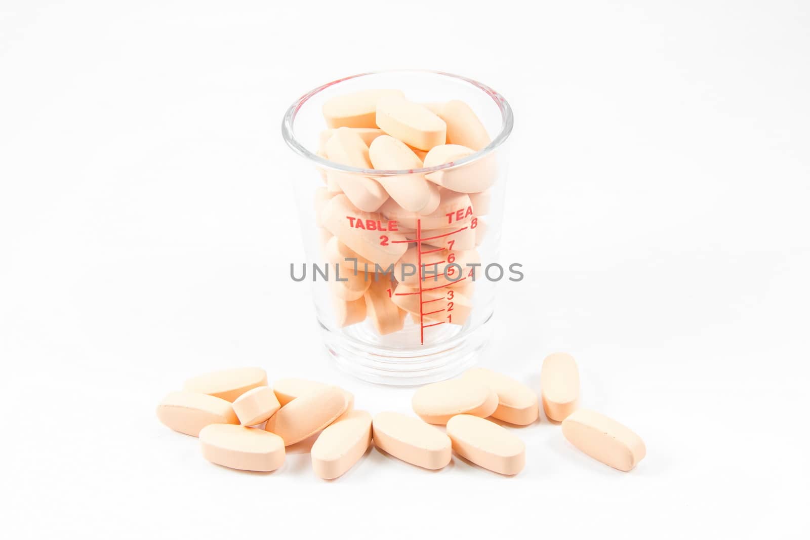 Medicine pills in glass measuring cup isolated on white background