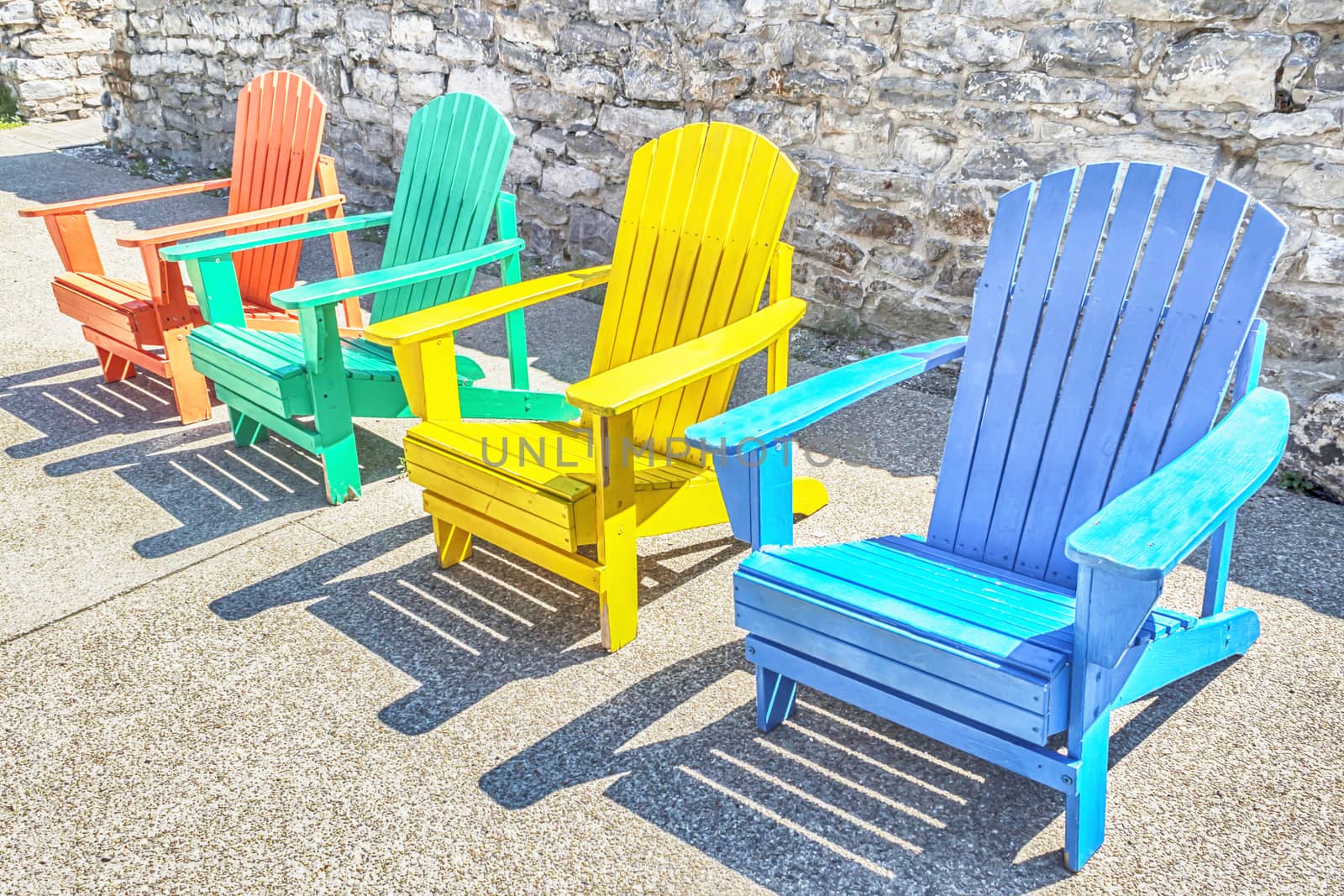 Brightly colored adirondack chairs arranged in a row. Bright sun lights them.