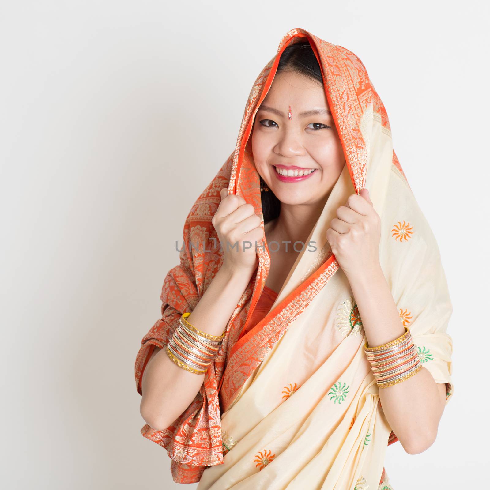 Portrait of Indian Muslim girl in sari covered her head, smiling confidently on grey background.