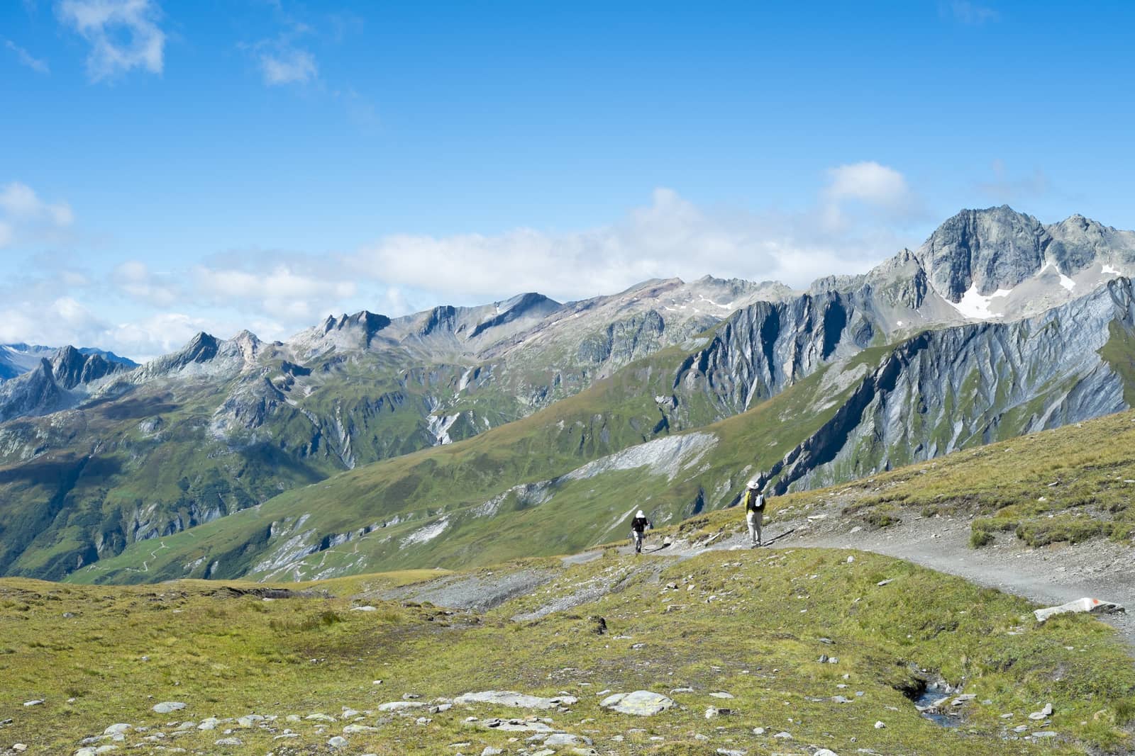 SEIGNE HILL, ITALY - AUGUST 27: Hikers on hill path with large peaks in the background. The region is a stage of the Mont Blanc tour, which crosses three countries. August 27, 2014 in Seigne Hill.