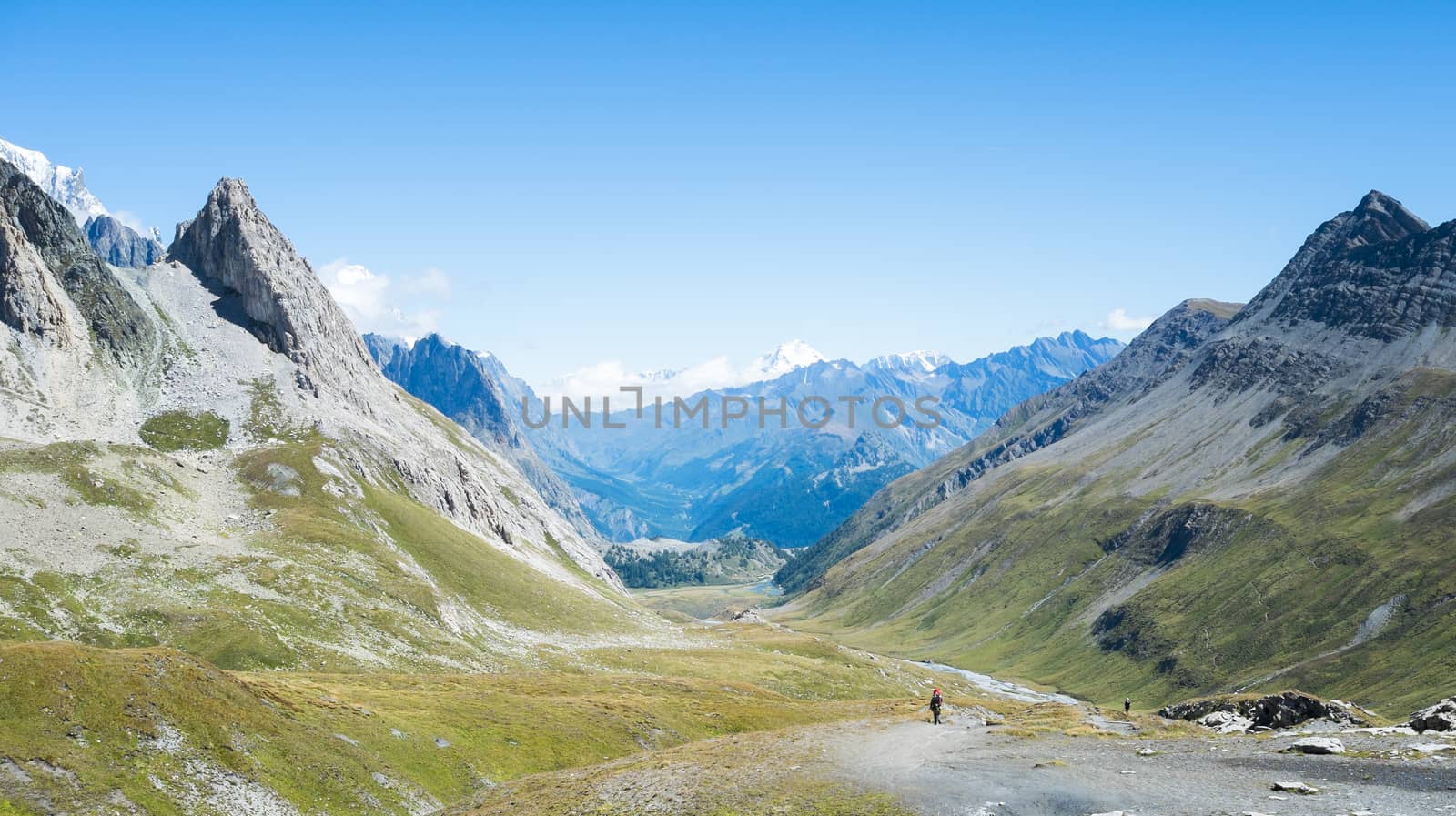 SEIGNE HILL, ITALY - AUGUST 27: Hikers on hill path with snowy Grand Combin mountain in the background. The region is a stage of the popular Mont Blanc tour. August 27, 2014 in Seigne Hill.