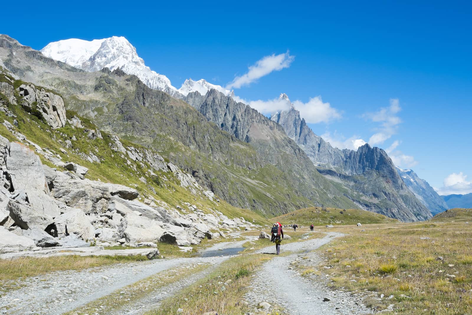 VAL VENY, ITALY - AUGUST 27: Hikers on valley path with Limestone Pyramids in the background. The region is a stage of the popular Mont Blanc tour. August 27, 2014 in Val Veny.