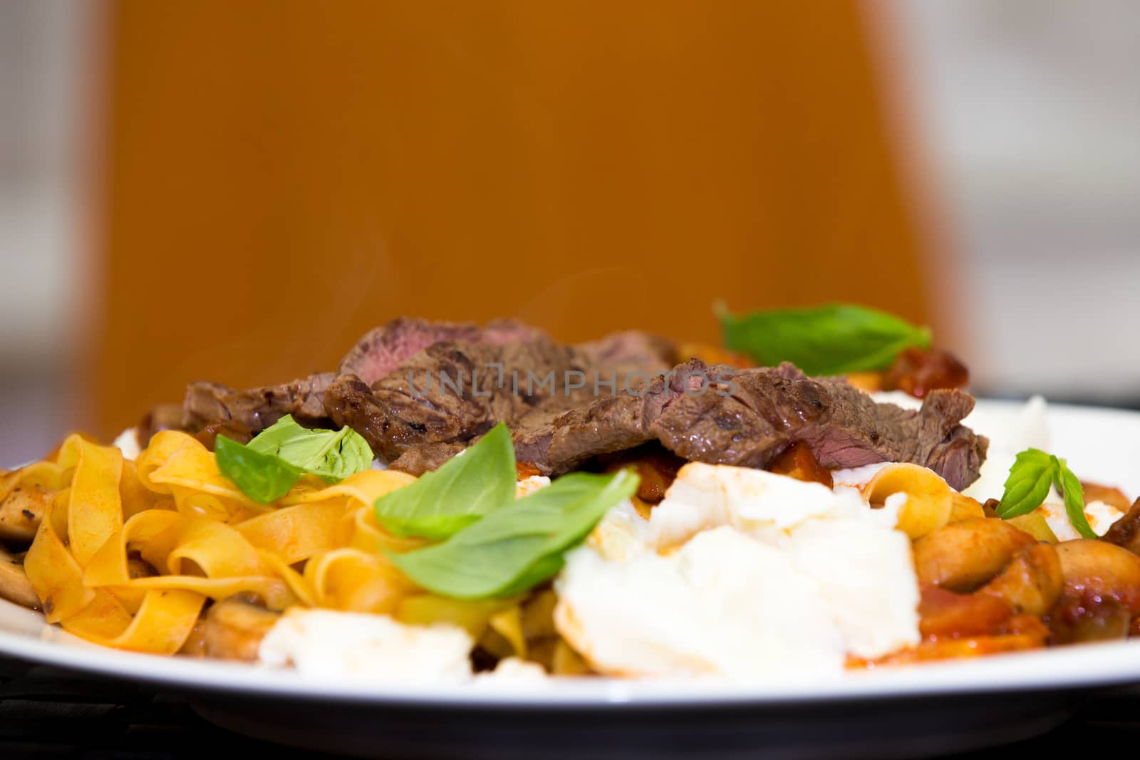 Serving of grilled beef steak and Italian pasta garnished with fresh basil leaves, low angle view