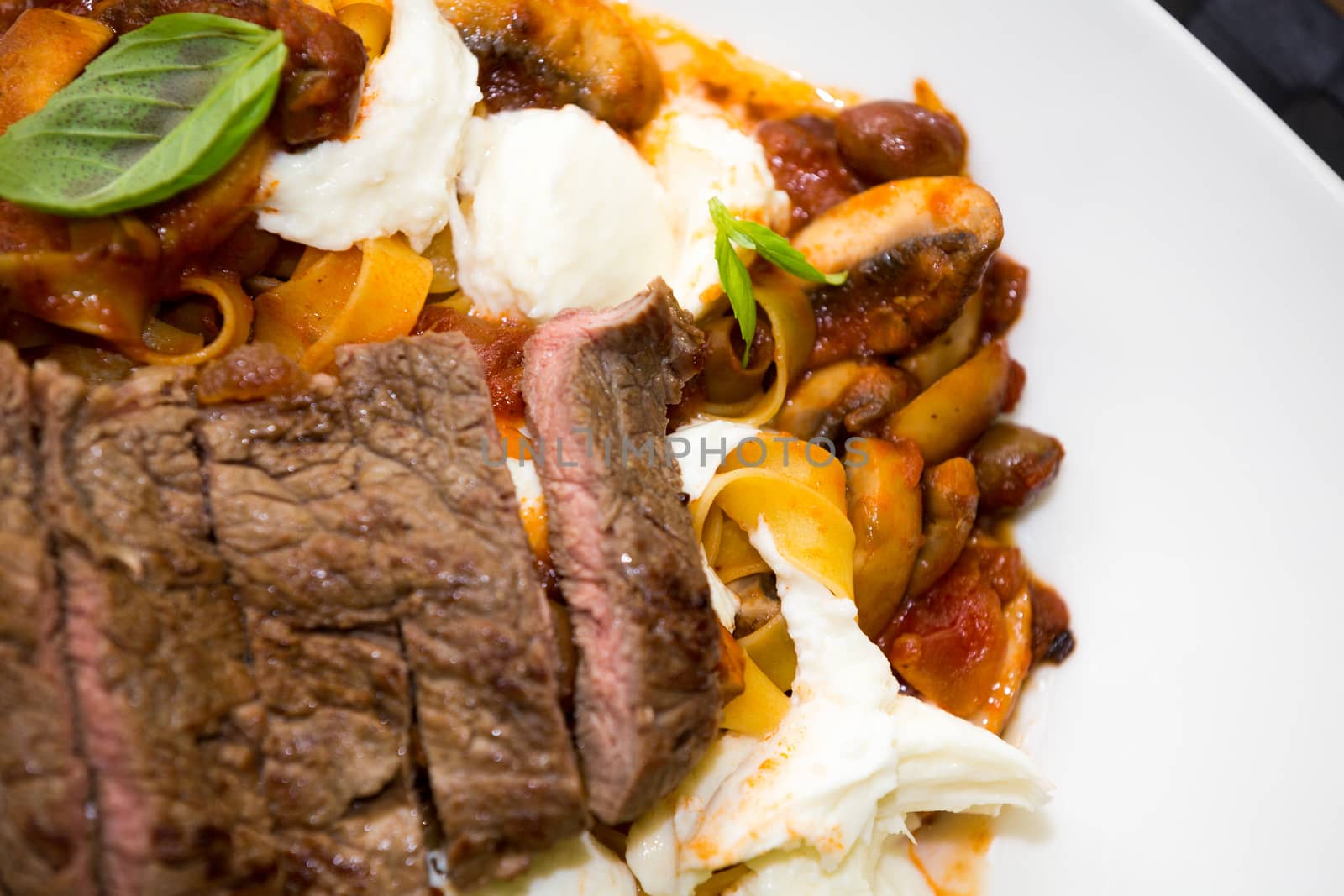 Overhead view of a serving of Italian ribbon pasta with sliced grilled beef steak seasoned with fresh basil on a plate