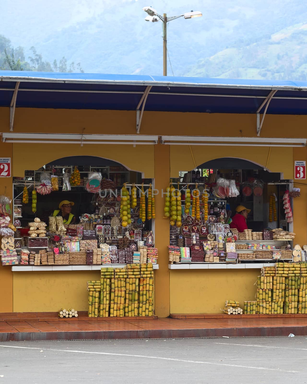 BANOS, ECUADOR - FEBRUARY 22, 2014: Unidentified people at small shops selling oranges, mandarins, sugarcane and sweets close to the bus terminal on February 22, 2014 in Banos, Ecuador. These stands are selling freshly cut sugarcane which can be eaten and is very juicy and the melcocha, which is a traditional taffy from Banos made of sugarcane.