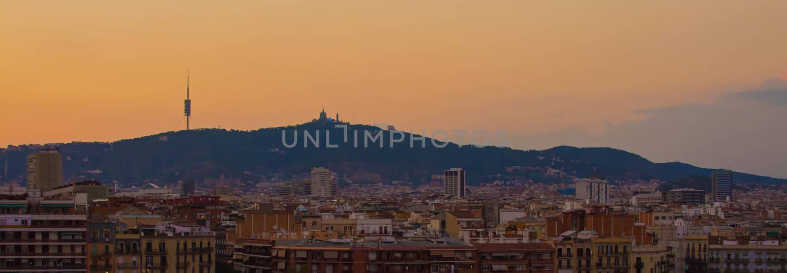 Panorama of Barcelona skyline, with buildings in the foreground and mountains in the background, at sunset