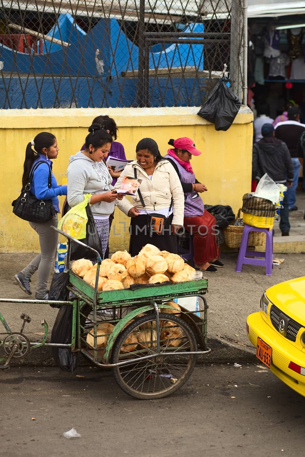 AMBATO, ECUADOR - MAY 12, 2014: Unidentified people on the sidewalk with a small cart of coconuts on the roadside on May 12, 2014 in Ambato, Ecuador.