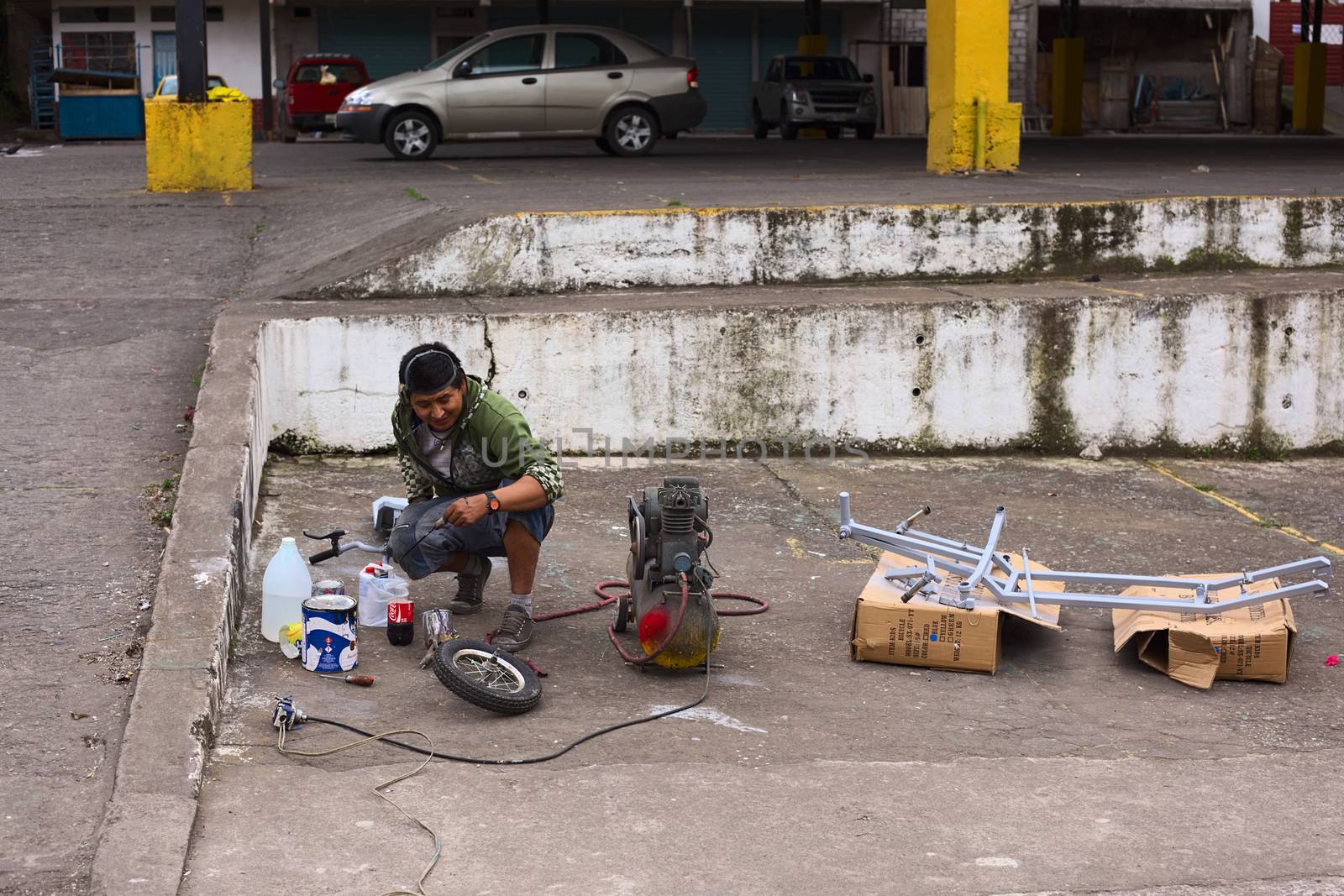 BANOS, ECUADOR - AUGUST 1, 2014: Unidentified person spraying a metal frame with grey color opposite a small bike repair shop on Juan Leon Mera street on August 1, 2014 in Banos, Ecuador. 