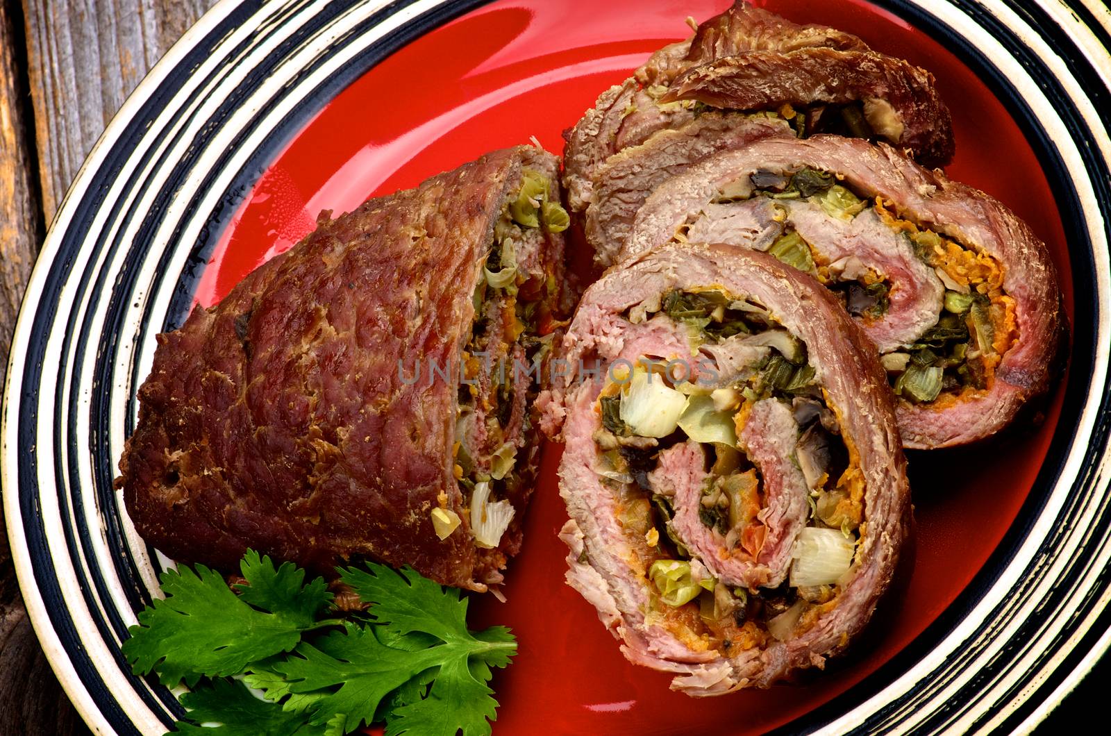 Rolled Beef Meatloaf Stuffed with Leek, Carrot and Greens Half and Slices on Red Plate