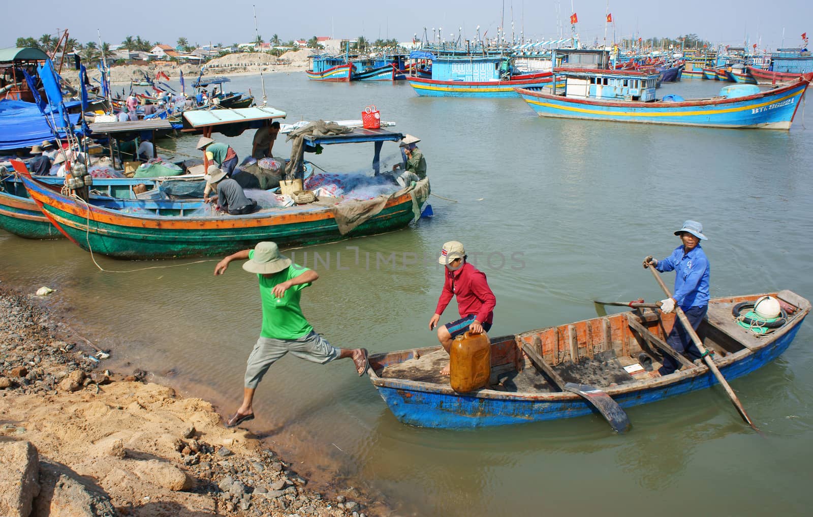 BINH THUAN, VIETNAM- JAN 20: Transportation people and goods by small wooden boat from fishing boat to shore, colorful fishing boat on habor on day at fishing village, Viet Nam, Jan 20, 2014