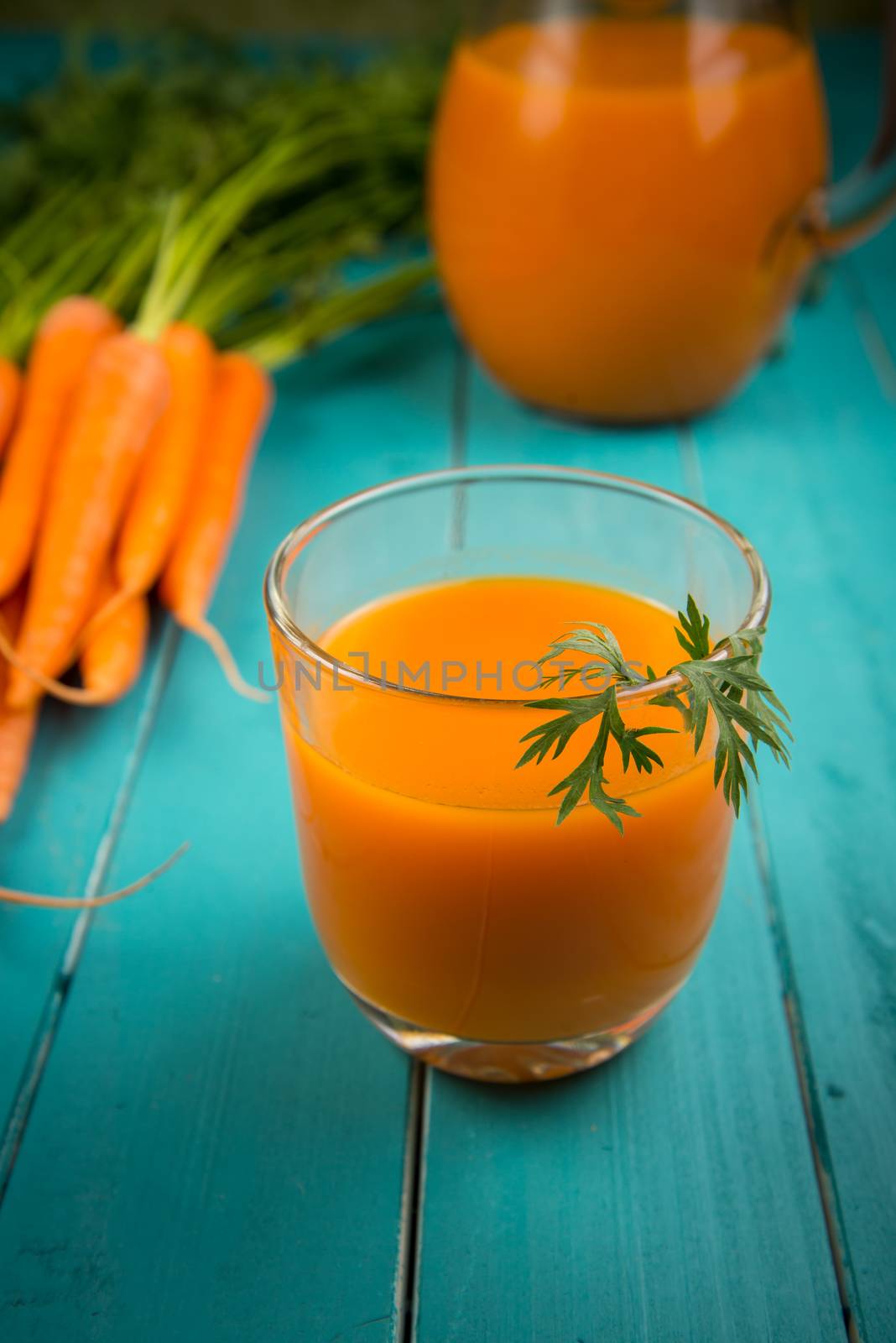 Homemade natural carrot juice in glass on rustic blue wooden table in background