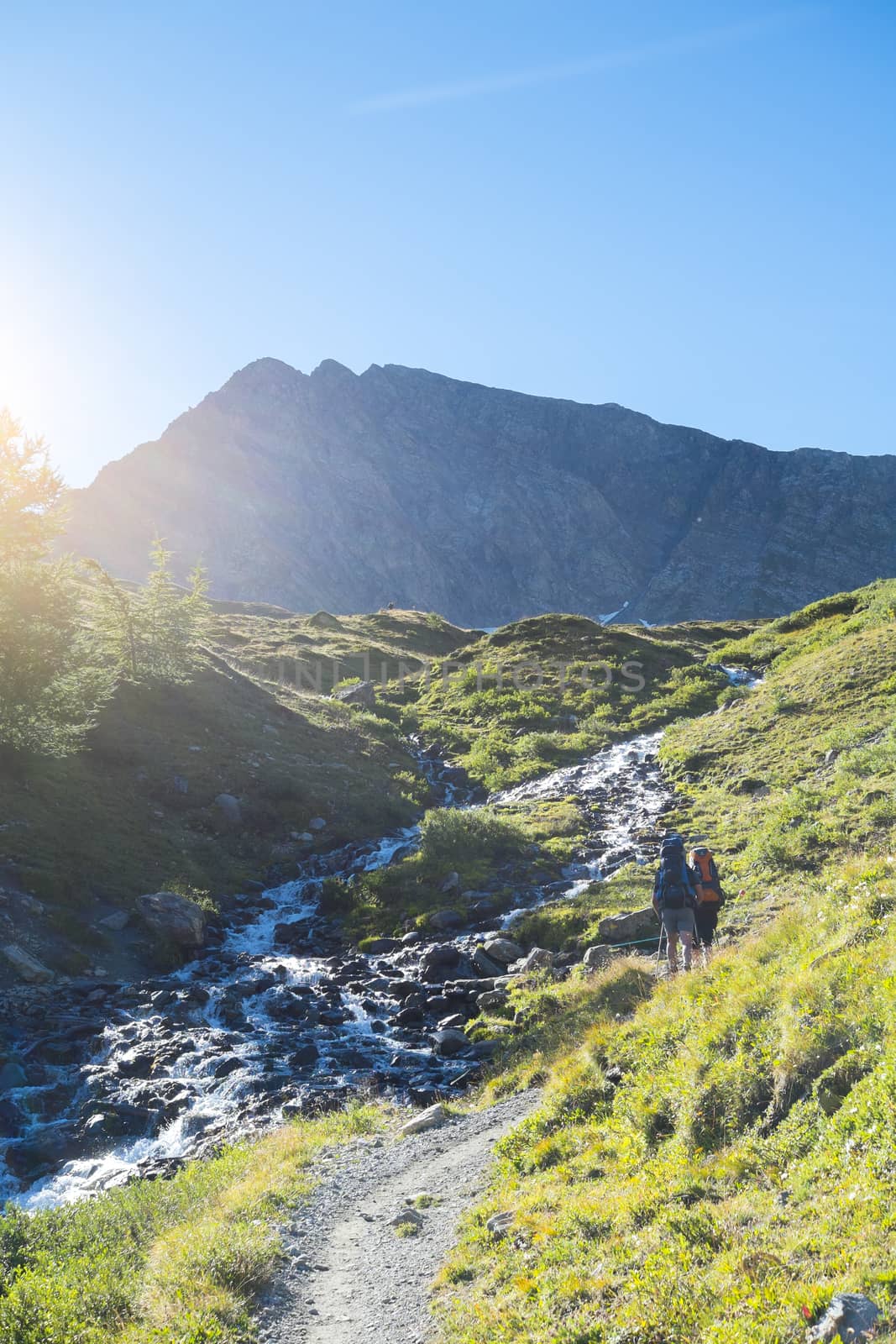 COMBAL, ITALY - AUGUST 28: Hikers walking up path by creek with Charmonts Peaks in the background. The area is on a stage of the popular European Mont Blanc tour. August 28, 2014 in Combal.