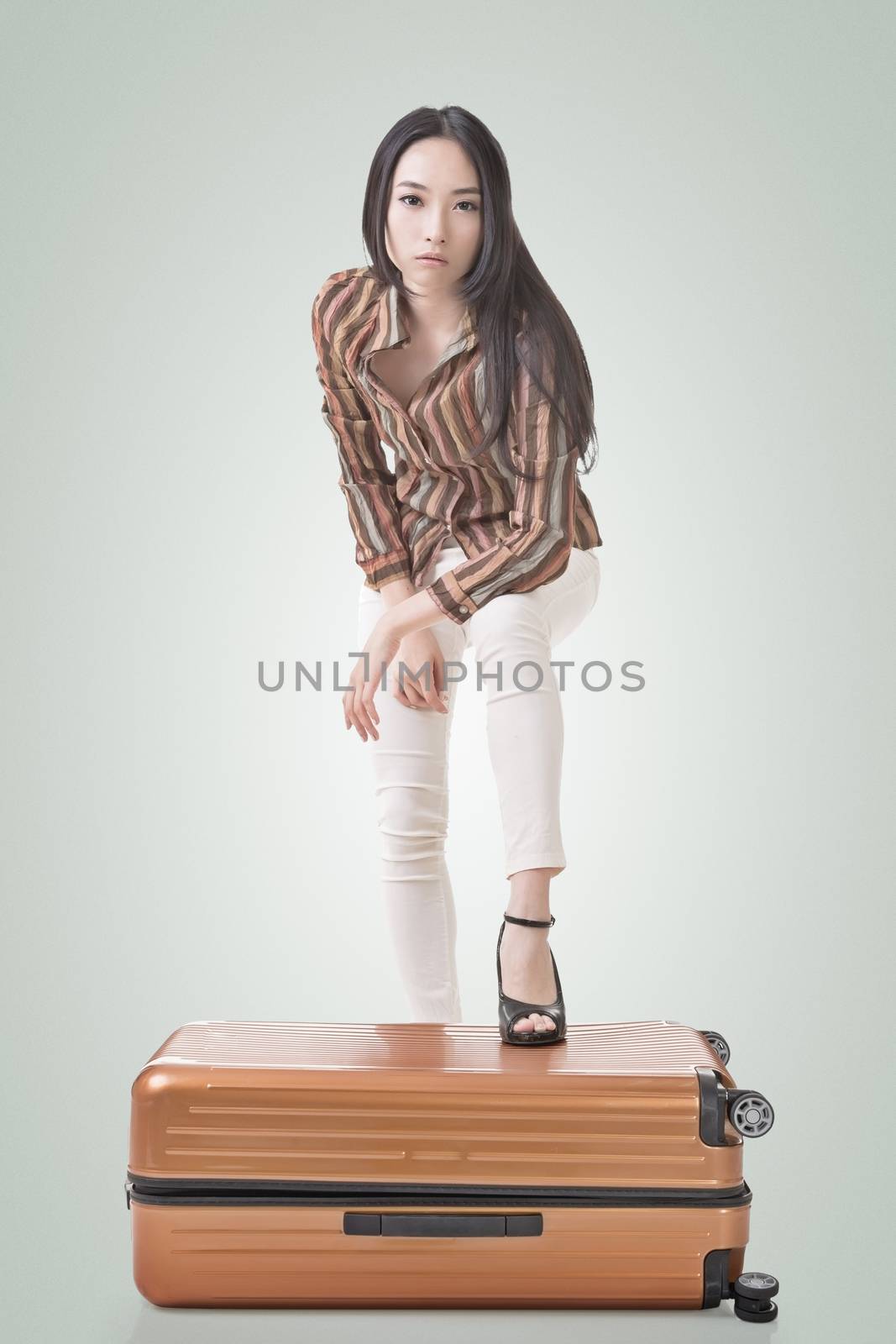 Modern Asian woman stand on a luggage, full length portrait on white background.