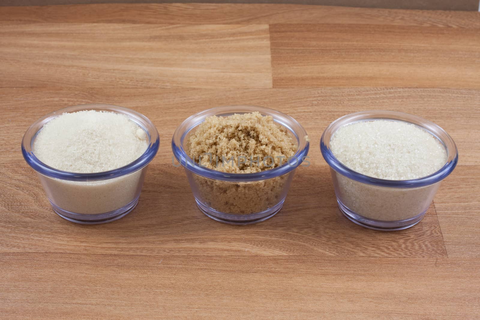 Organic crystal, brown, and fine sugar in clear bowls on a wooden surface.