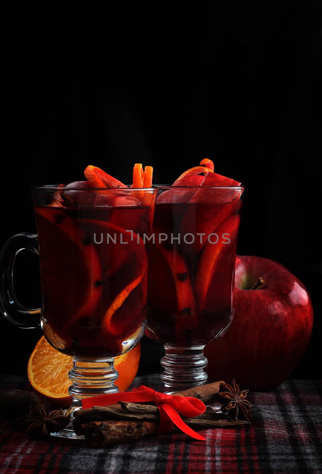 Hot red mulled wine with fruits and cinnamon on checkered tablecloth